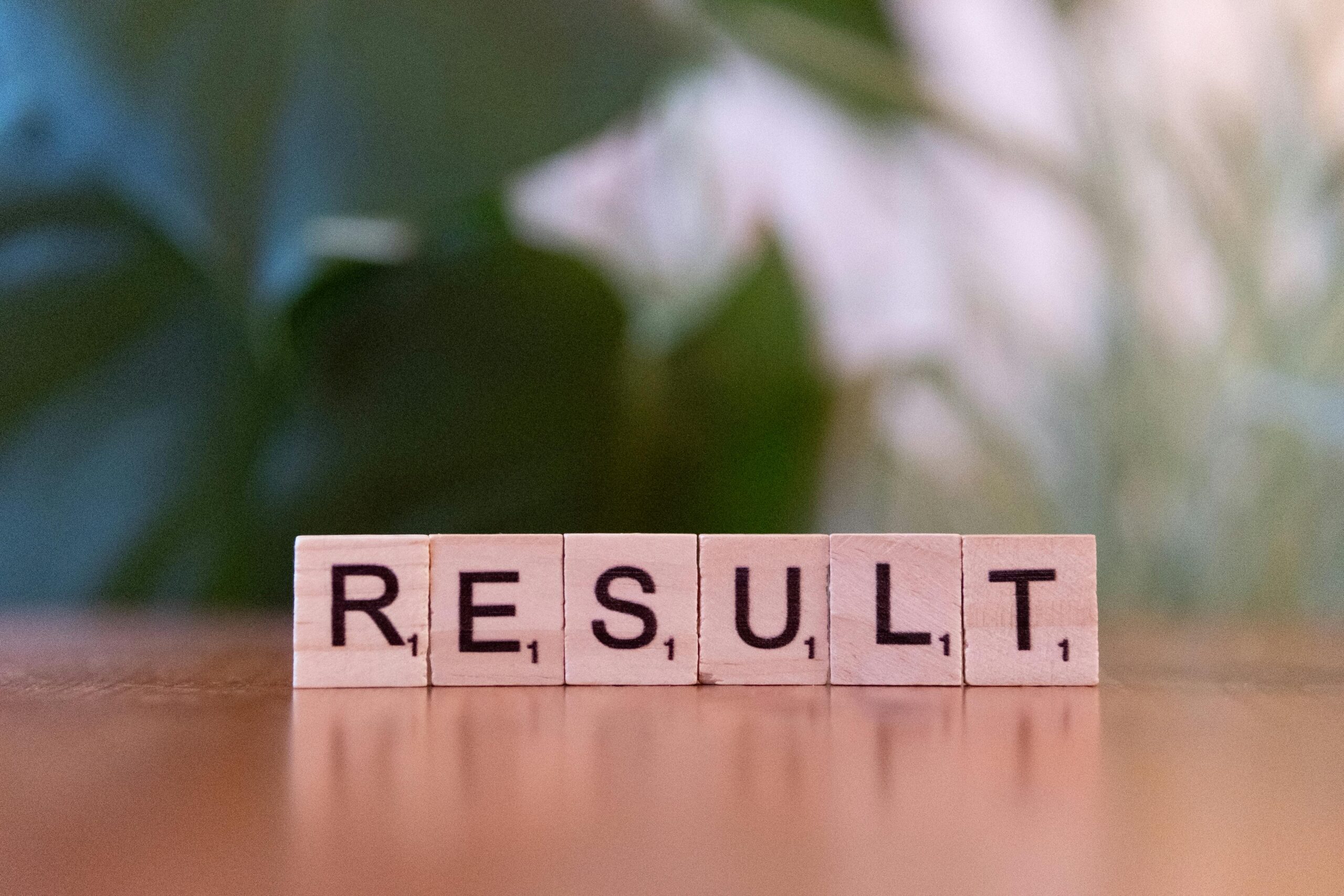 Wooden scrabble tiles arranged to spell RESULT on a wooden table.